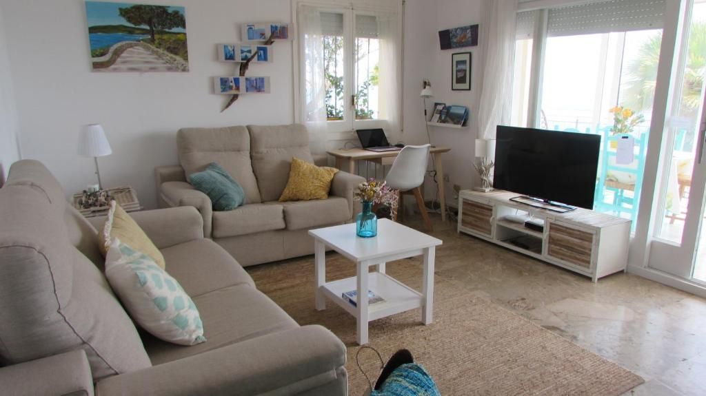 Sala de estar luminosa con sofás beige, mesa de centro blanca, televisor y puertas corredizas de vidrio.