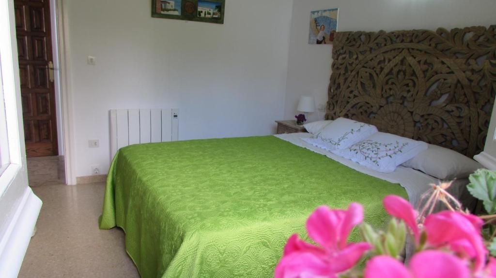 Habitación luminosa con una colcha verde, cabecero estampado y flores rosas en primer plano.