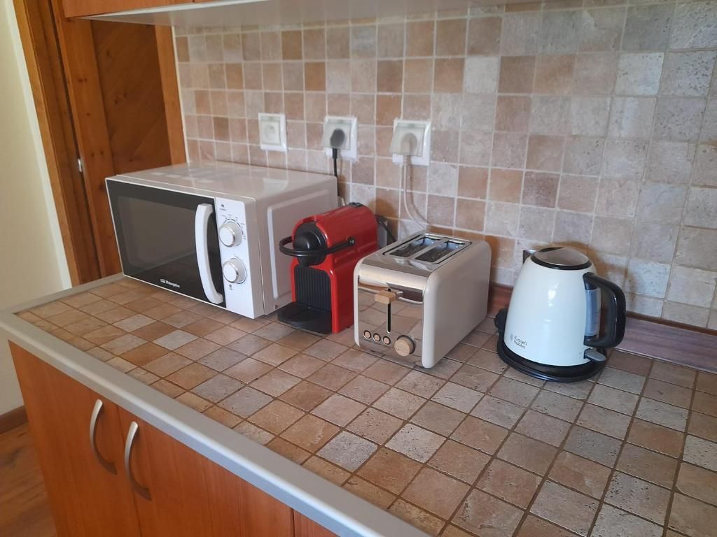Encimera de cocina con microondas, cafetera roja, tostadora y hervidor eléctrico contra un salpicadero de azulejos.