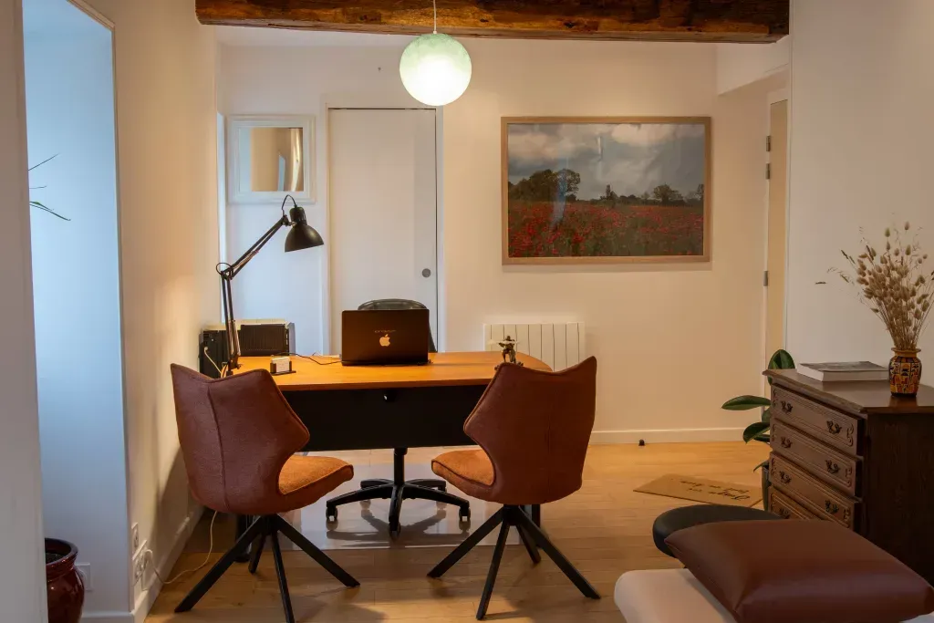Un salon avec un bureau et des chaises et un ordinateur portable dessus.