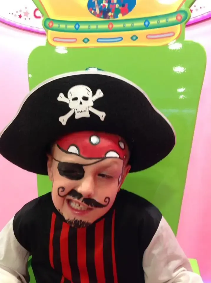 Niño disfrazado de pirata con pintura facial, sombrero y parche en el ojo, sonriendo.