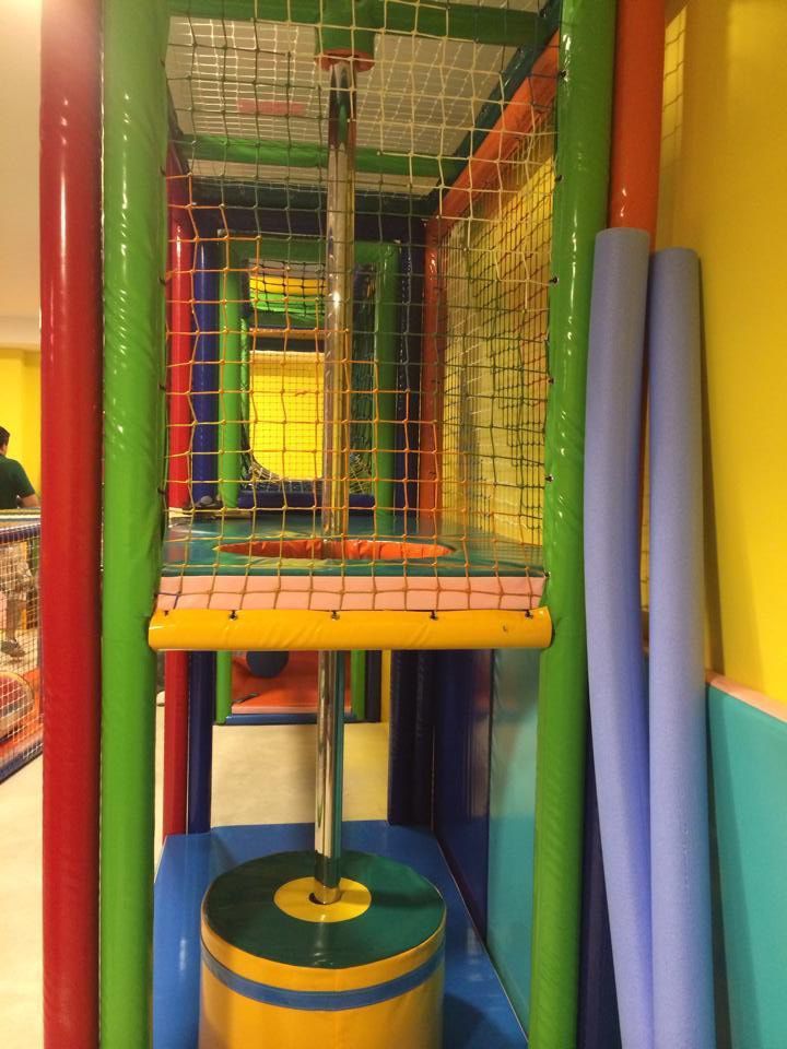 Estructura de juego de interior con columnas de colores, red y un obstáculo cilíndrico.