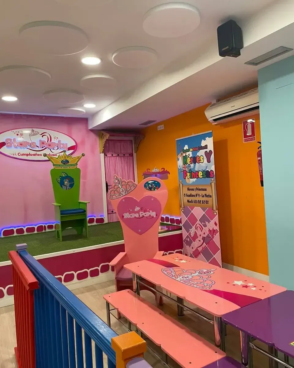 Sala de juegos con paredes de colores, mesas y un trono.