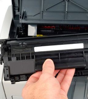 Mano retirando un cartucho de tóner negro de una impresora láser.