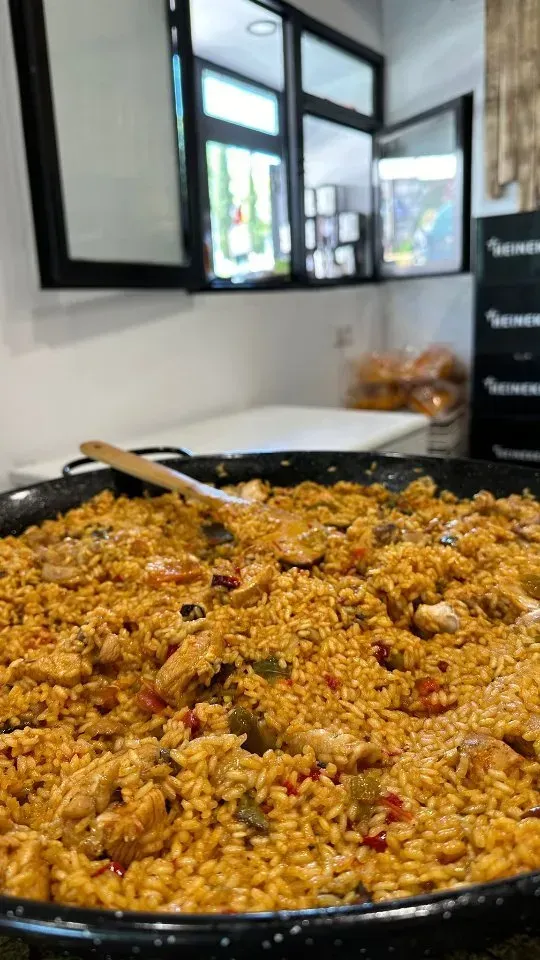 Una sartén llena de arroz y carne con una cuchara de madera dentro.