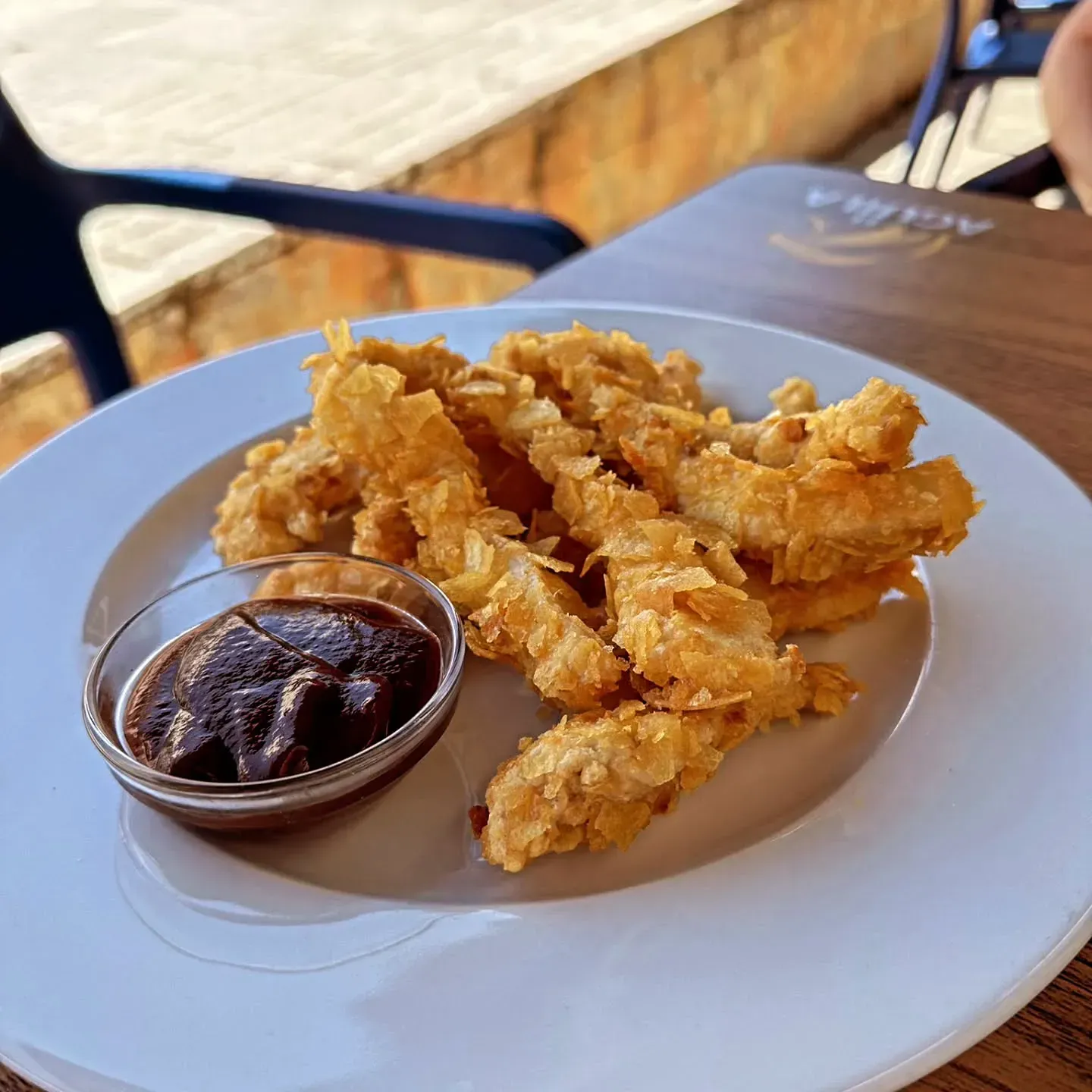 Un plato blanco cubierto con pollo frito y salsa sobre una mesa de madera.