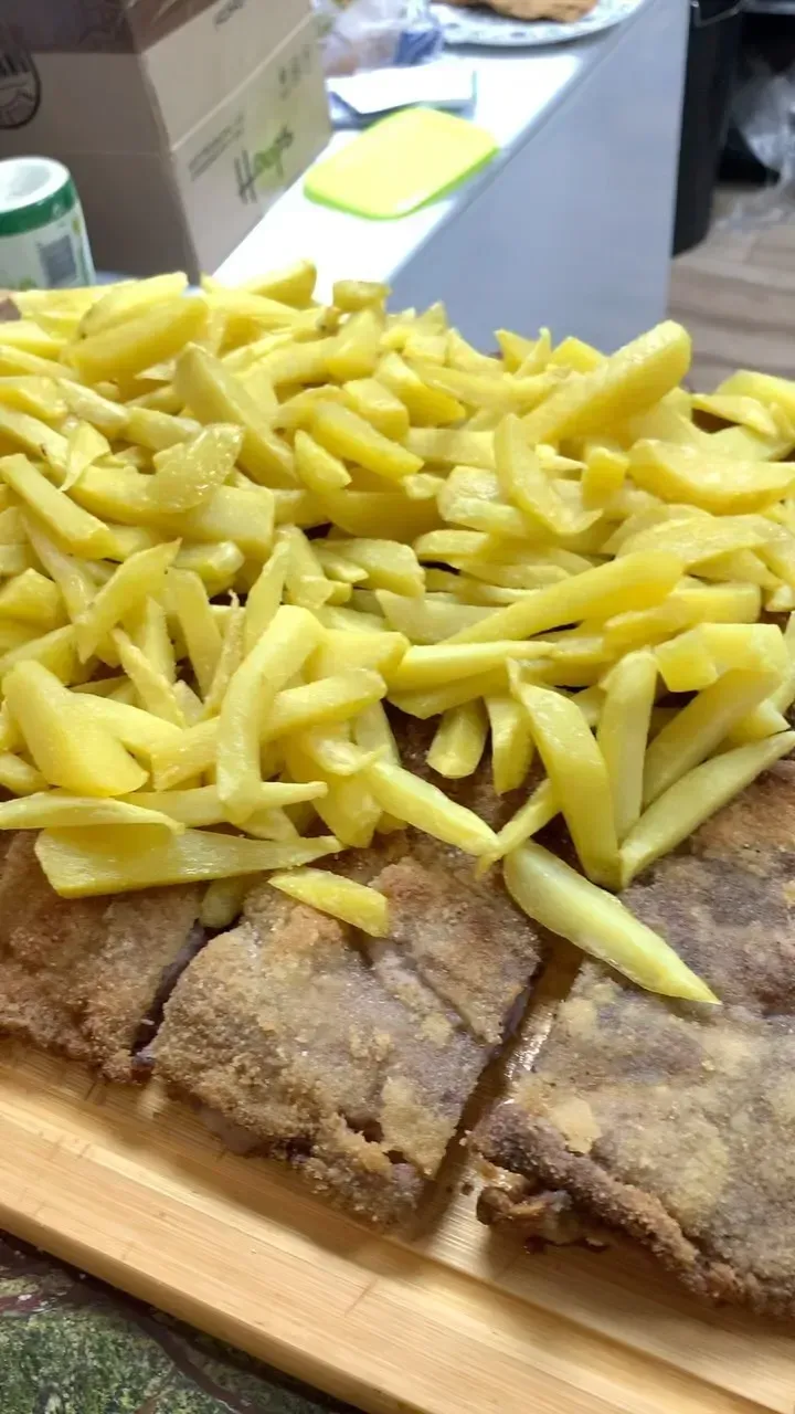 Una tabla de cortar de madera cubierta con papas fritas y carne.