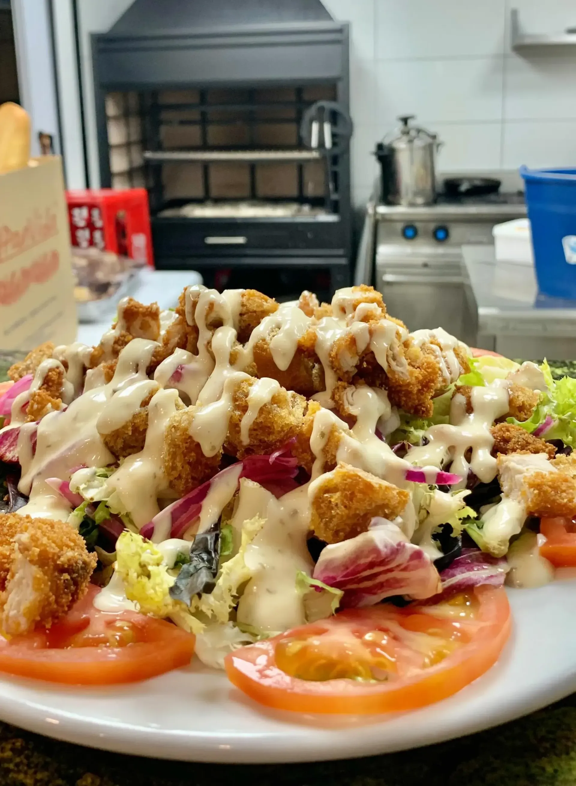 Un plato blanco cubierto con ensalada y tomates en una cocina.
