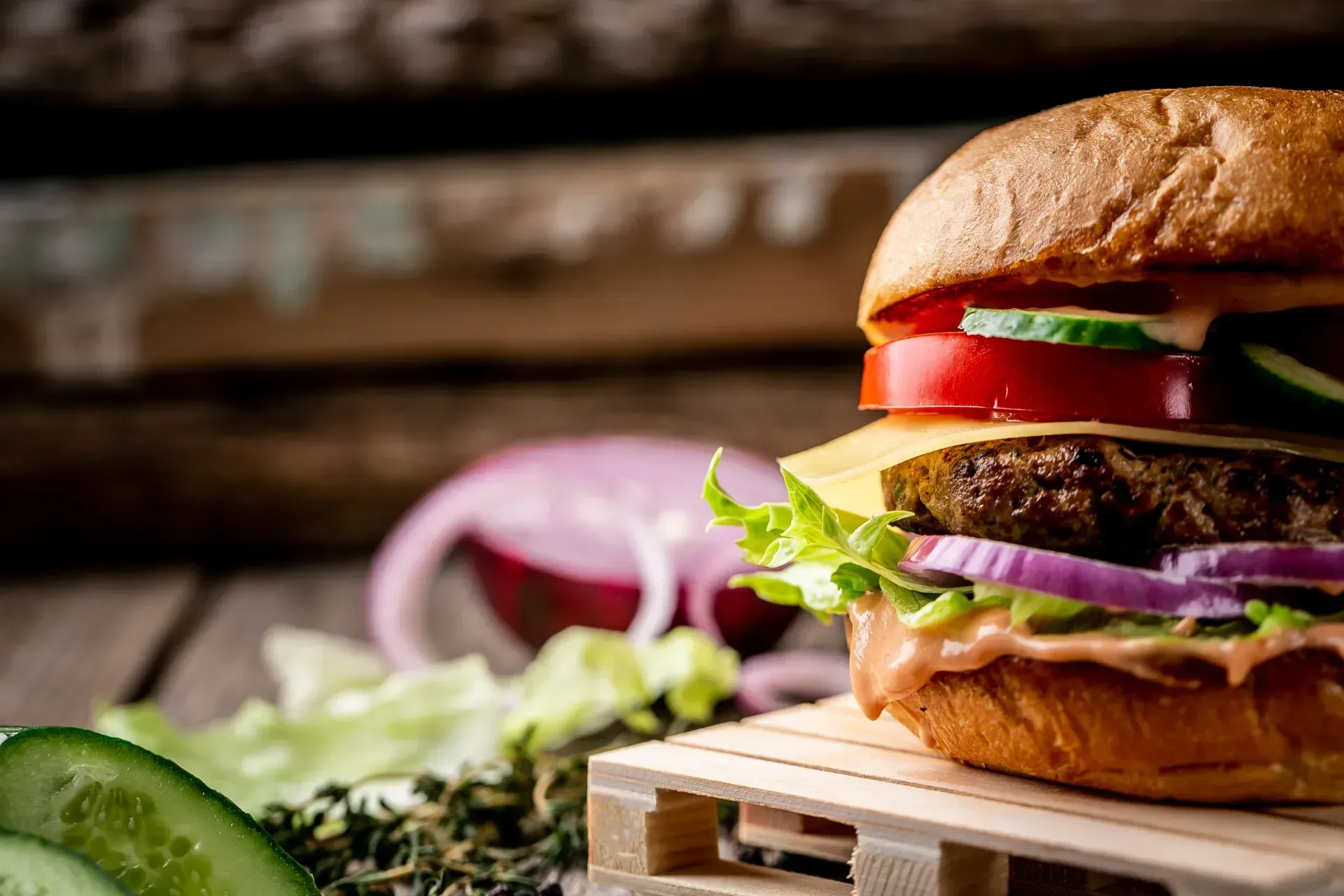Una hamburguesa está sentada sobre una paleta de madera sobre una mesa de madera.