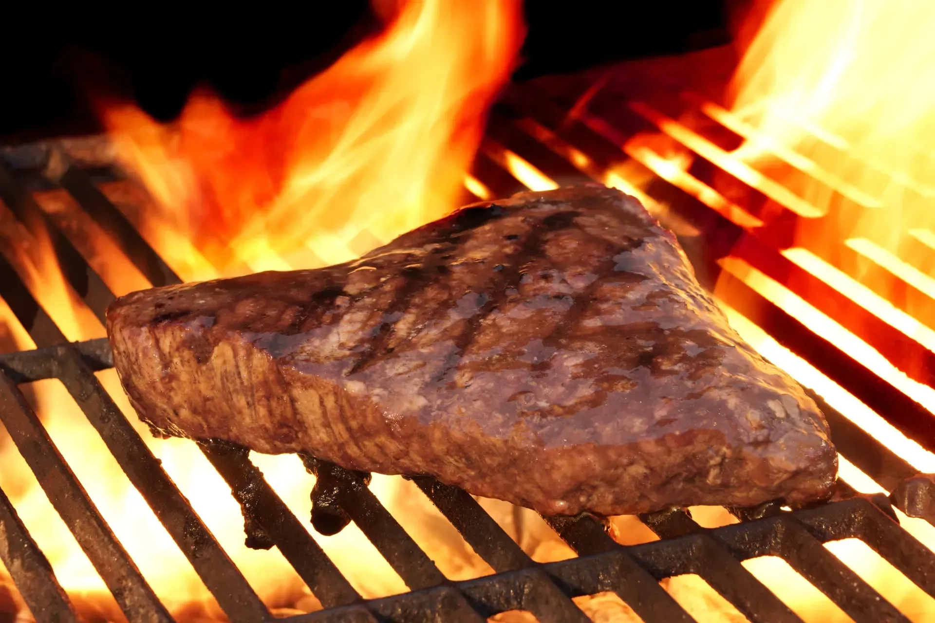 Un filete se está cocinando en una parrilla con llamas detrás de él.