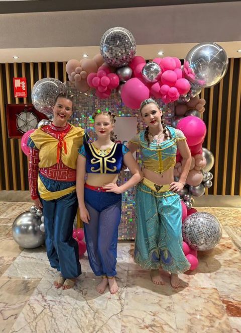 Three girls in costume are posing for a picture in front of balloons.