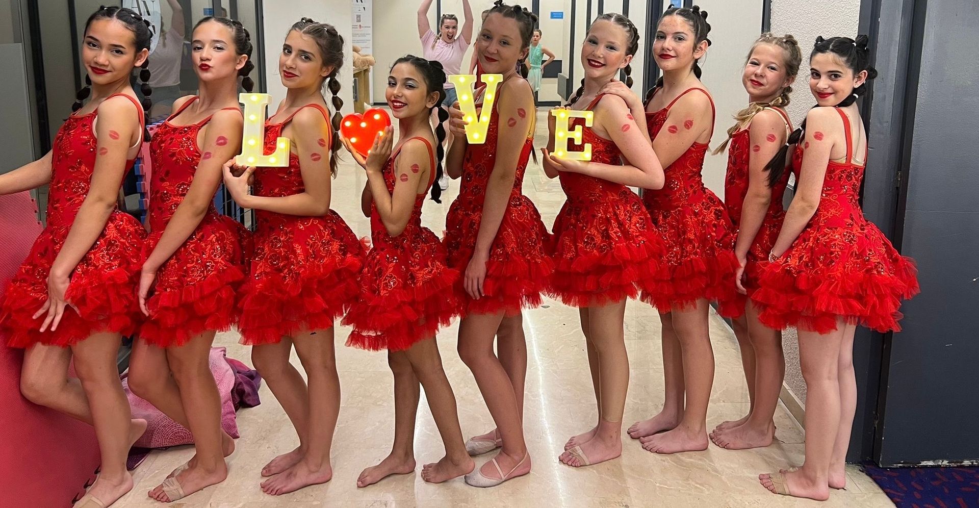 A group of young girls in red dresses are standing next to each other in a room.