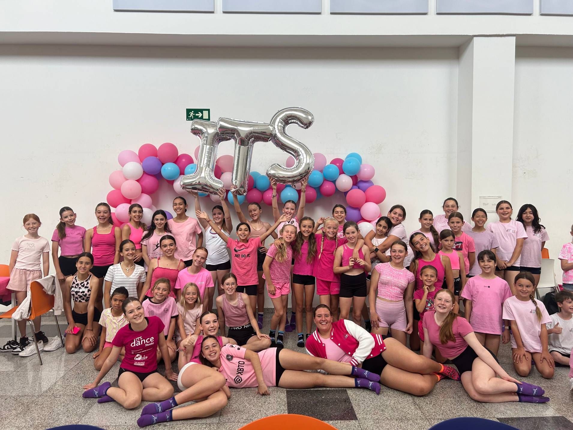 A group of young girls are posing for a picture in front of balloons.