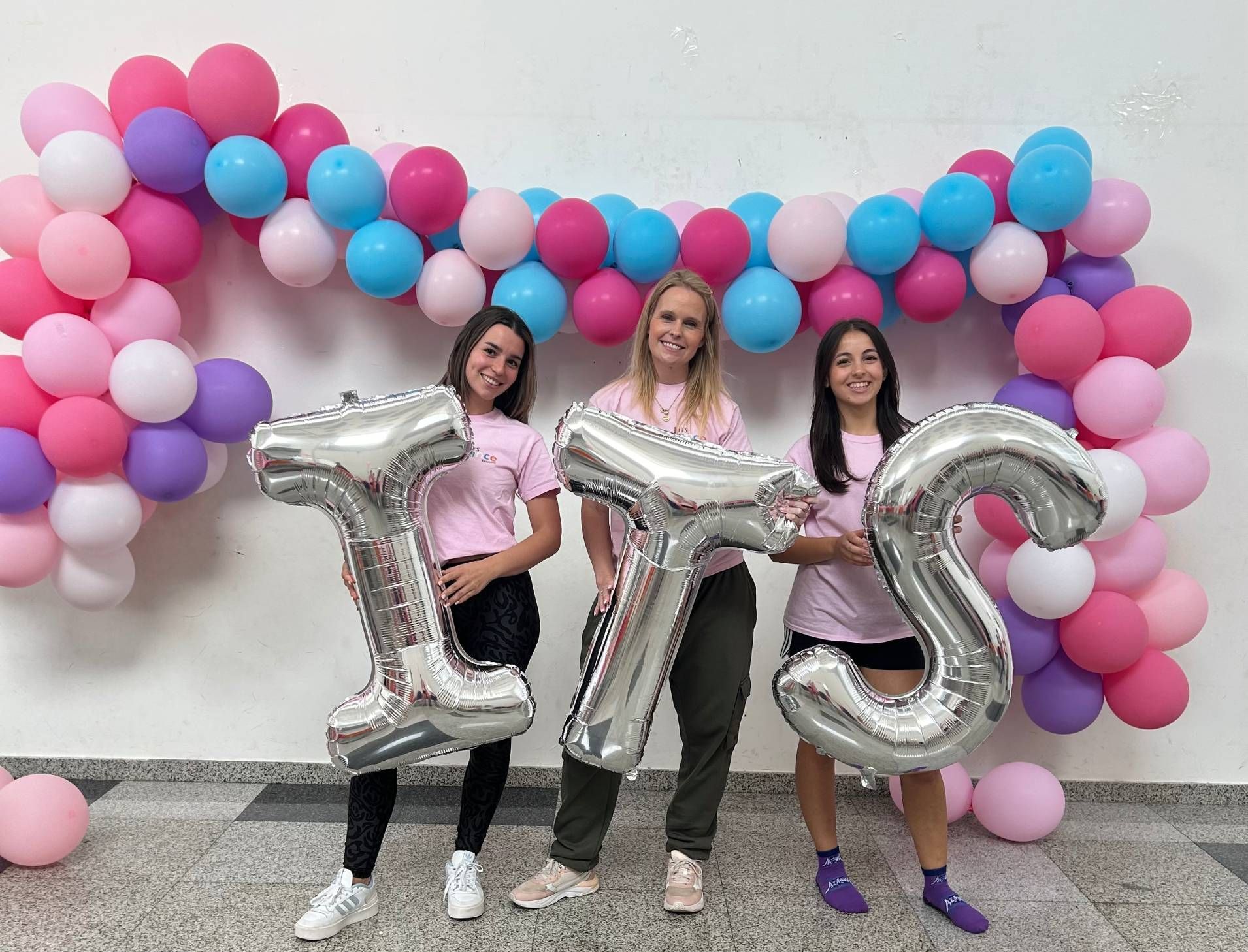 Three women are holding balloons that spell out the word it 's.