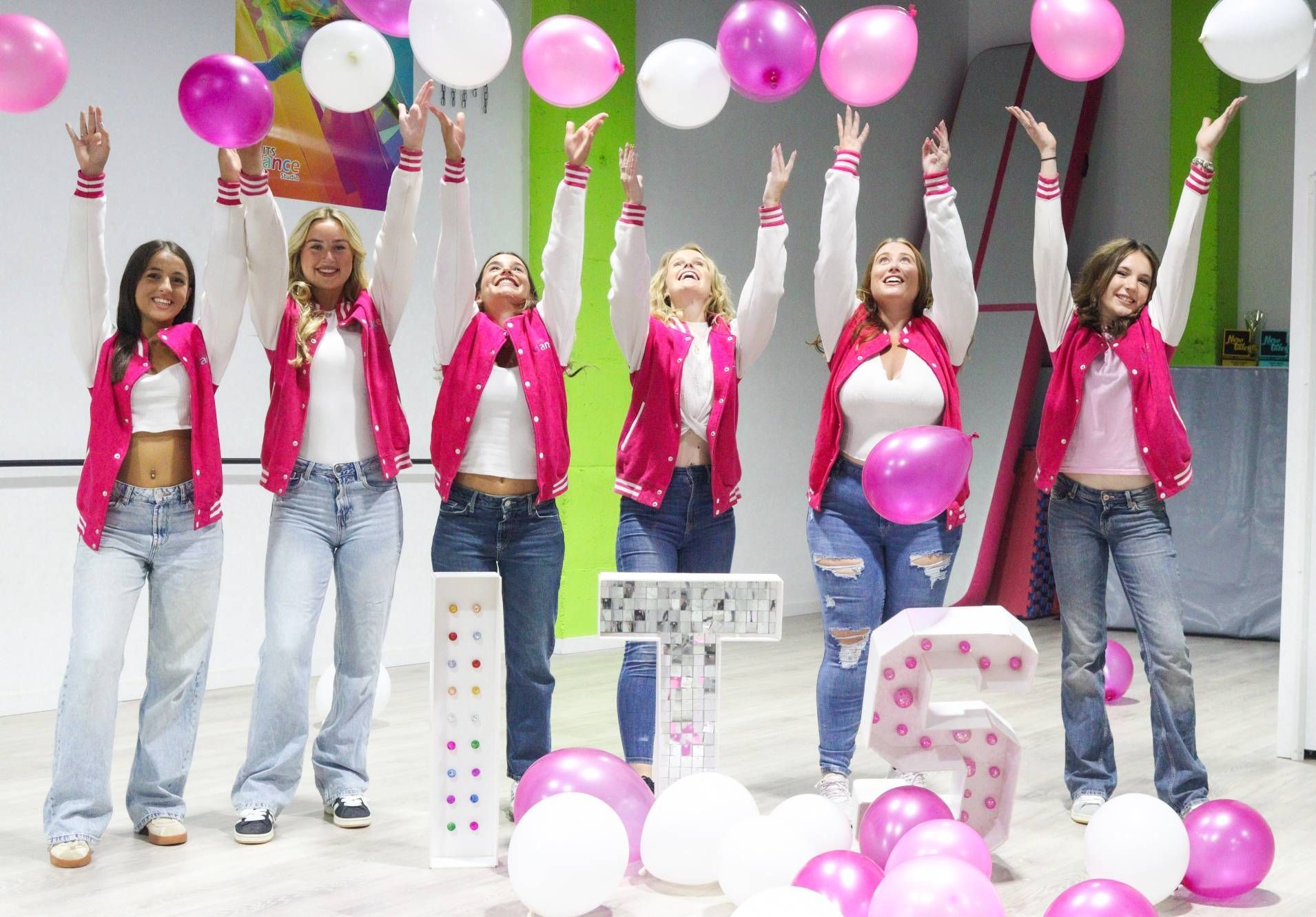 A group of women are standing next to each other holding pink and white balloons.