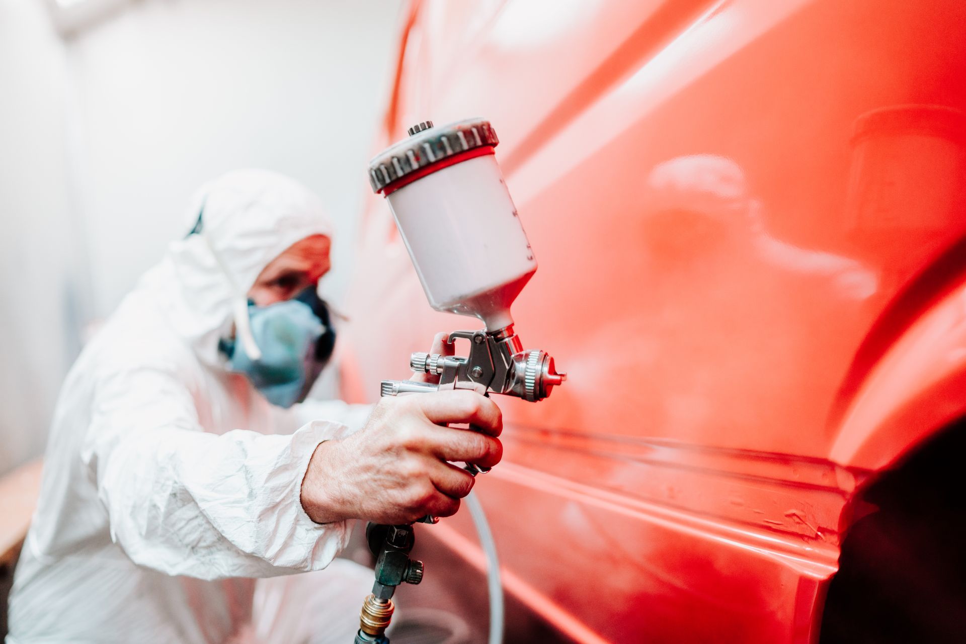 Carrossier qui peint un véhicule dans une cabine de peinture