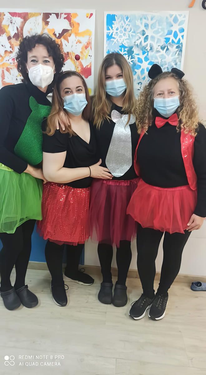 Cuatro personas disfrazadas y con máscaras: una mujer con corbata verde y falda de lentejuelas rojas, otras con corbatas y faldas de tutú.