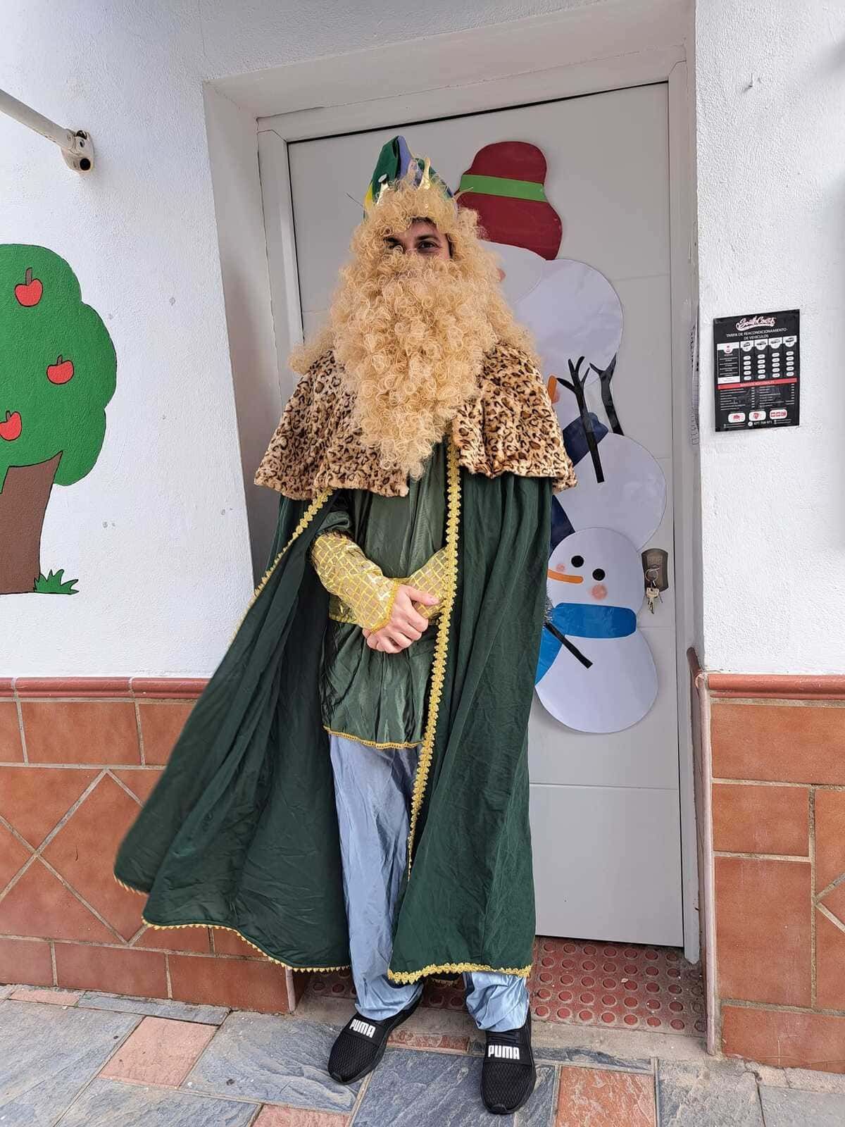Un hombre vestido de rey con una capa verde se encuentra afuera de una puerta blanca decorada con muñecos de nieve.