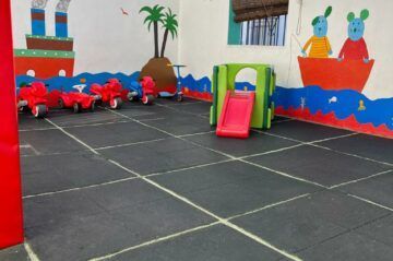 Sala de juegos con vehículos de juguete y tobogán sobre suelo de baldosas. Decoraciones murales pintadas.