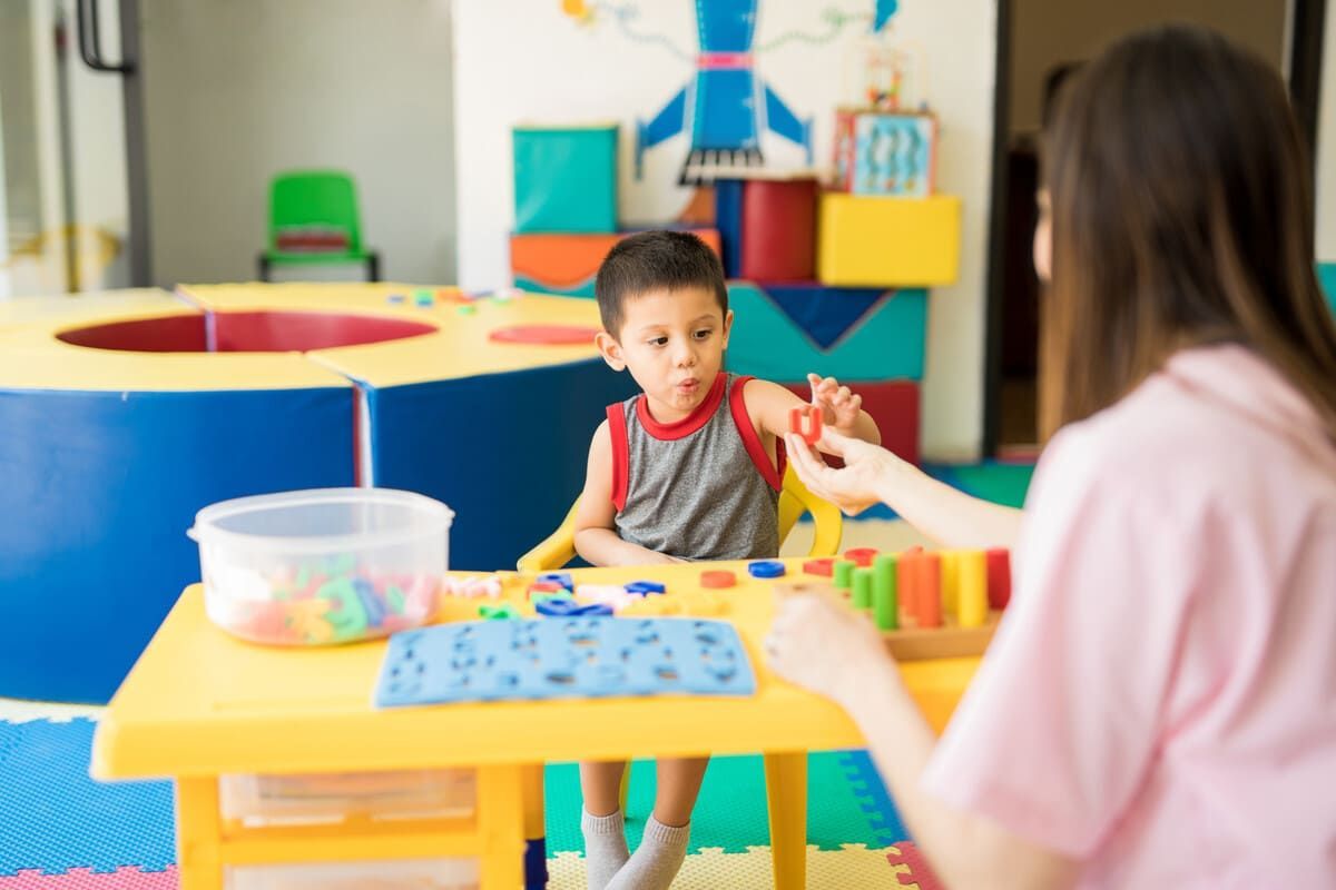 Un niño pequeño y su cuidador juegan con bloques de colores en una mesa en una sala de juegos de colores brillantes.
