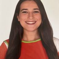 Mujer con cabello largo y oscuro, sonriente, vistiendo una blusa roja y blanca con un borde verde, sobre un fondo blanco.