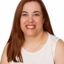 Mujer con cabello largo rojizo sonriendo, vistiendo una camiseta blanca sin mangas, sobre un fondo blanco.