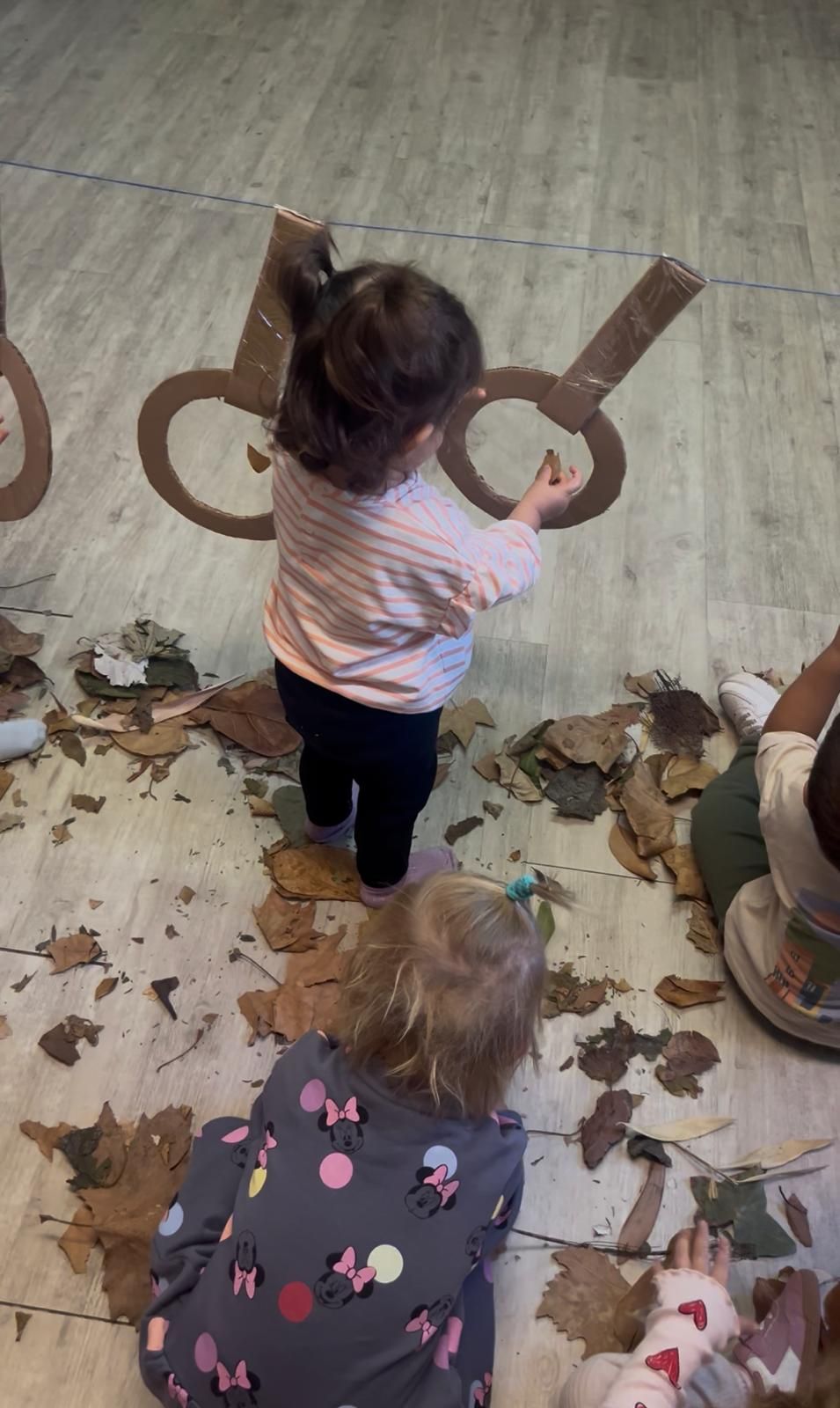Dos niños pintan hojas de otoño en una mesa. Se ven paletas y pinceles.