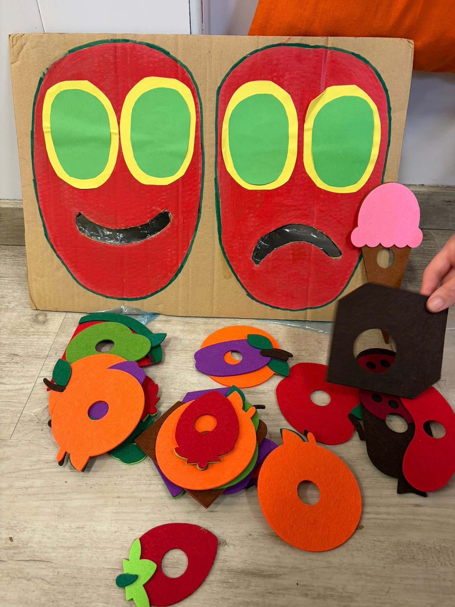 Cuatro niños pequeños en una mesa en una guardería, algunos comiendo, con juguetes coloridos en el fondo.
