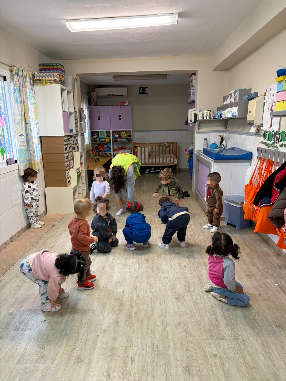 Niños jugando en una sala de juegos colorida con una cocina de juguete, juguetes mecedores y una pelota.