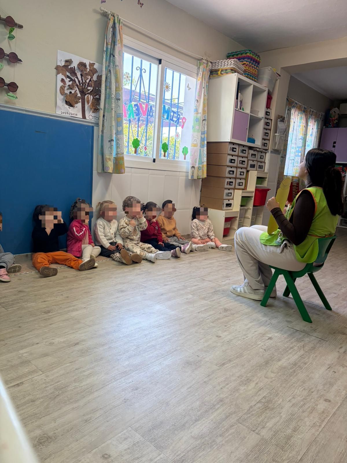 Maestra y niños jugando con bloques y dibujando en el suelo en un aula colorida.