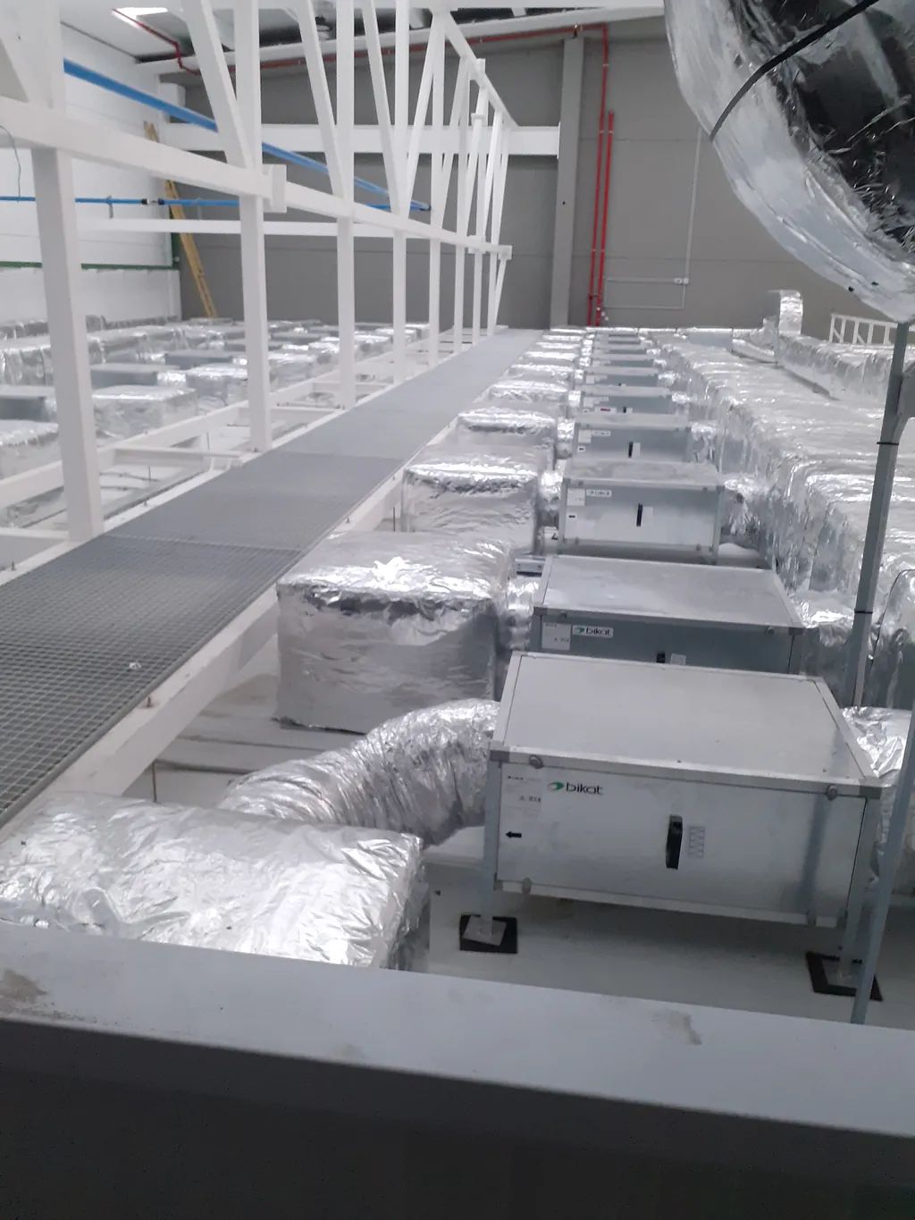 Un técnico con una camiseta gris de marca trabaja en bombas industriales azules dentro de una sala de máquinas.