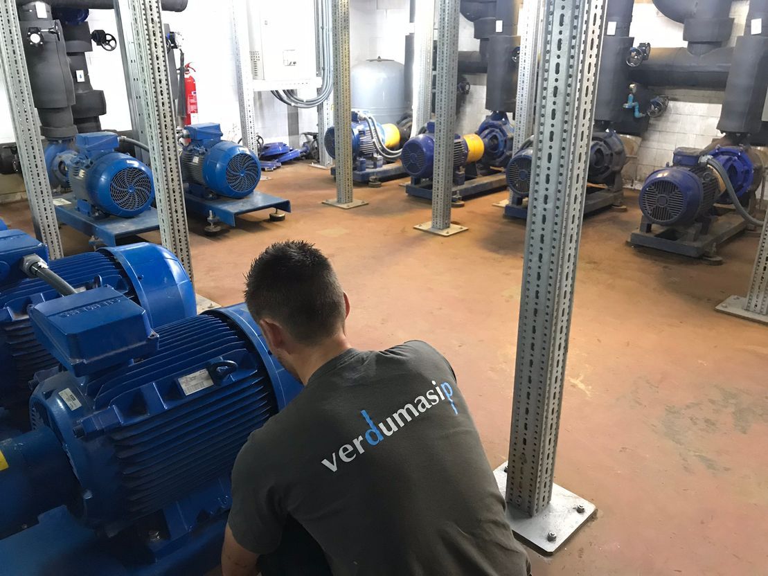 Un técnico con una camiseta gris de marca trabaja en bombas industriales azules dentro de una sala de máquinas.