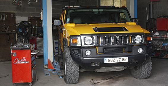 Un SUV Hummer H2 jaune à l'intérieur d'un garage, probablement en réparation.