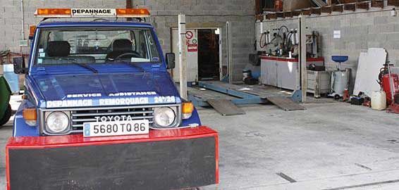 Camion de dépannage Toyota bleu dans un garage avec pont élévateur.