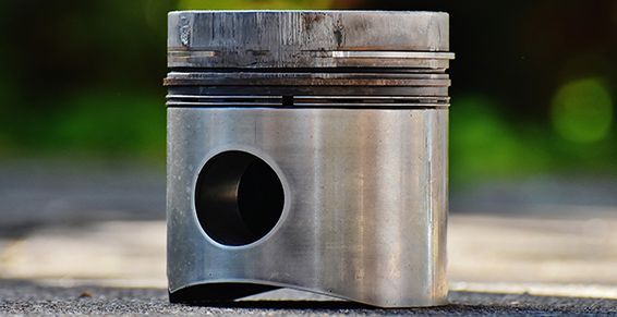 Piston argenté avec une partie supérieure foncée, un trou circulaire et des rainures visibles.