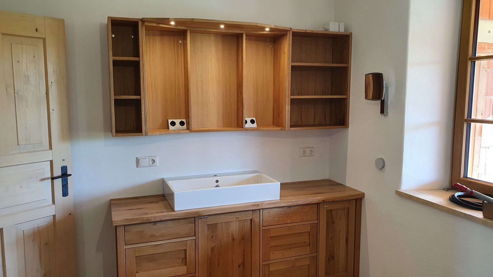 Innenansicht einer Holztreppe, die zu einem Wohnbereich mit Fenstern und hoher Decke führt.