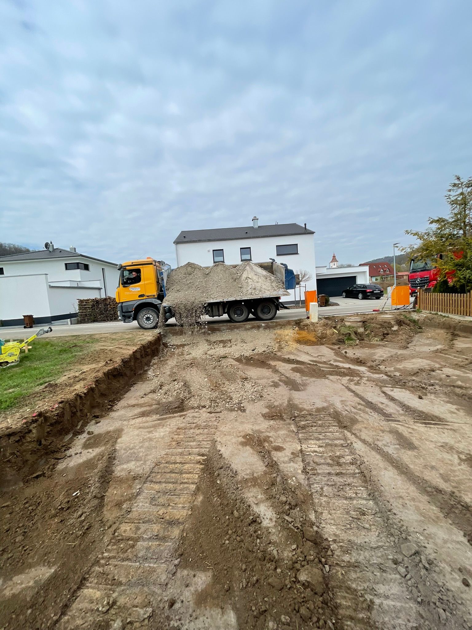 Baustelle mit Erdhaufen und Baumaschine vor Wohnhaus