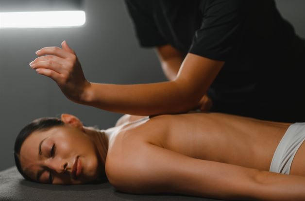 Persona recibiendo masaje de espalda en un entorno oscuro. El terapeuta utiliza el codo.