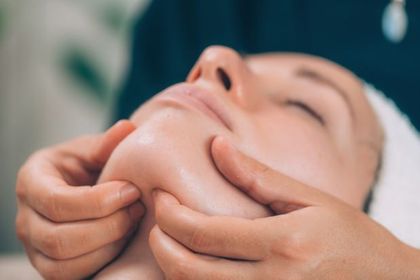 Mujer recibiendo un masaje facial en la barbilla. Las manos aplican presión en la mandíbula.