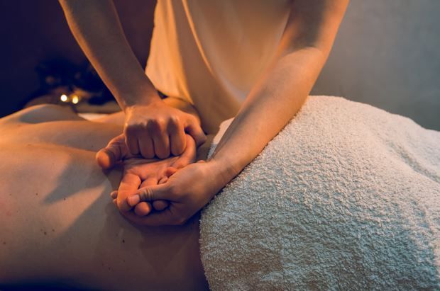 Manos proporcionando un masaje de espalda a una persona acostada sobre una toalla.