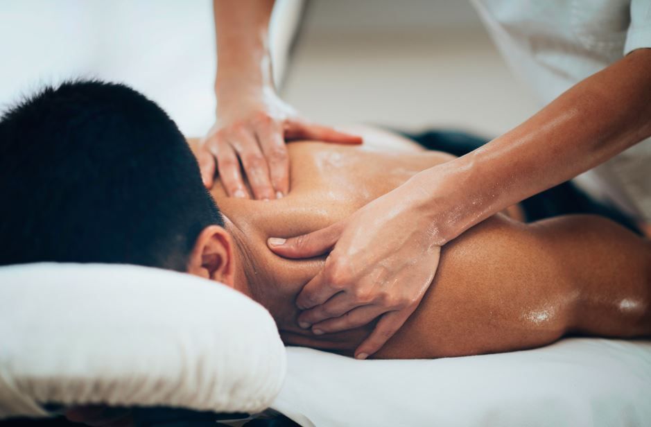 Manos dando un masaje de espalda a una persona acostada boca abajo en una mesa de masajes.