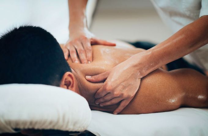 Manos dando un masaje de espalda a una persona acostada boca abajo en una mesa de masajes.