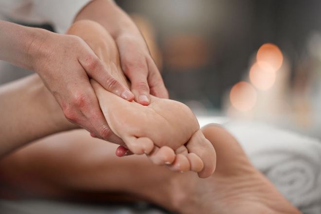 Manos masajeando la planta del pie, en el interior, iluminación suave, entorno de spa relajante.