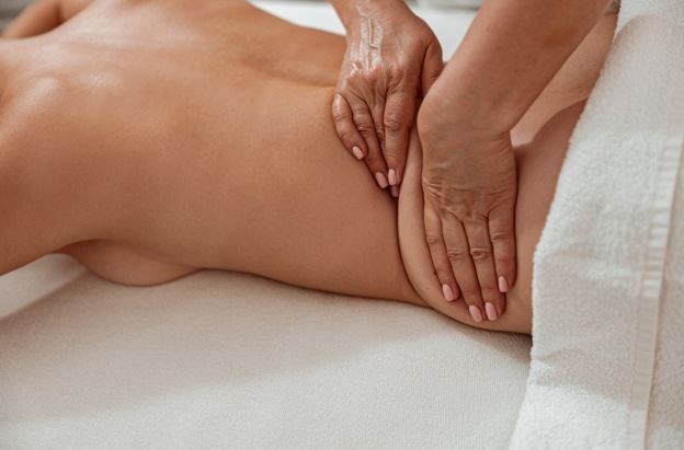 Manos masajeando la espalda baja y la cadera de una persona mientras está acostada sobre una superficie blanca.