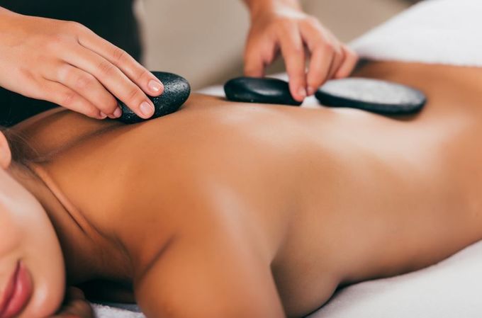 Persona recibiendo un masaje con piedras calientes en la espalda, manos colocando las piedras.