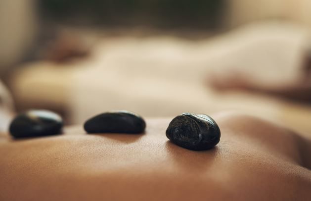 Tres piedras de masaje oscuras en la espalda de una persona; fondo borroso de otra persona.