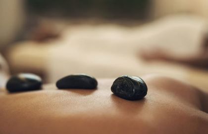 Tres piedras de masaje oscuras en la espalda de una persona; fondo borroso de otra persona.