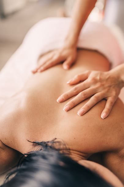 Manos masajeando la espalda de una persona en una mesa de masajes, cubierta con una toalla rosa.