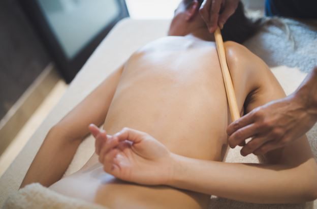 Persona recibiendo un masaje con bambú en la espalda mientras está acostada en una mesa de masajes.