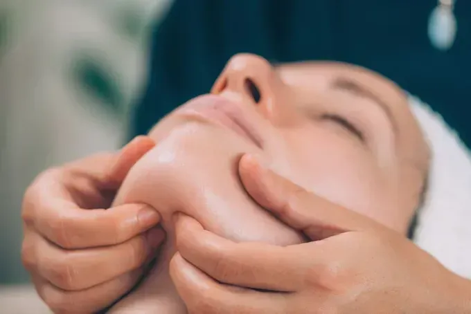 Manos masajeando el rostro de una persona durante un tratamiento facial en un spa.